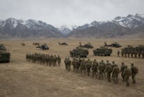 Military training exercise with helicopters and armored vehicles on field with mountain backdrop