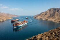Container ships passing through a strategic maritime corridor with desert coastline in background